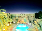 Outdoor pool glowing blue at night surrounded by desert-style architecture and palm trees at Hotel Ksar Merzouga