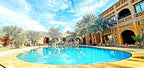 Hotel Ksar Merzouga outdoor swimming pool with blue water surrounded by palm trees and tan stone building under a blue sky