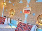 Hotel Ksar Merzouga rustic room interior with textured earth-toned walls, blue geometric accents, patterned cushions, and warm lighting