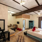 Hotel Nomad Palace cozy guest room with rustic Moroccan decor, white and beige walls, wooden beams, twin beds with red towels, lounge area, and patterned rug