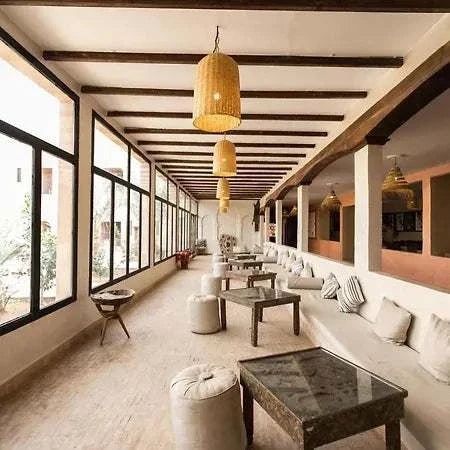 Hotel Nomad Palace indoor lounge area with beige cushions, wooden tables, wicker pendant lights, and large windows along one side