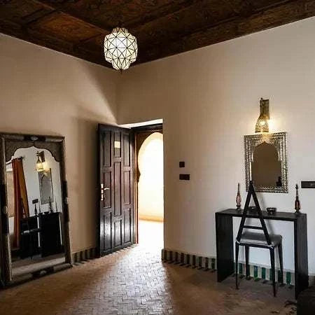 Hotel Nomad Palace Moroccan-style room with patterned wooden ceiling, decorative mirror, dark wooden door, and simple furnishing