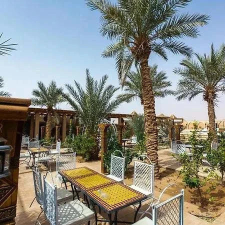 Outdoor dining area at Hotel Nomad Palace featuring mosaic tile tables, white wrought iron chairs, and palm trees