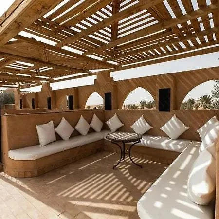 Hotel Nomad Palace outdoor seating area with curved beige stone benches, white cushions, a small round table, and wooden pergola overhead