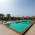 Outdoor swimming pool at Hotel Nomad Palace with turquoise water, beige stone tiles, sun loungers, and palm trees surrounding the area