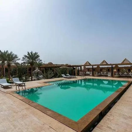 Outdoor swimming pool at Hotel Nomad Palace with turquoise water, beige stone tiles, sun loungers, and palm trees surrounding the area