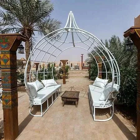 Outdoor seating area at Hotel Nomad Palace with white metal frame gazebo, white cushioned benches, and wooden coffee table