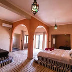 Hotel Nomad Palace room with mosaic tiled flooring, peach-colored walls, arched doorways, patterned beds, and hanging lanterns