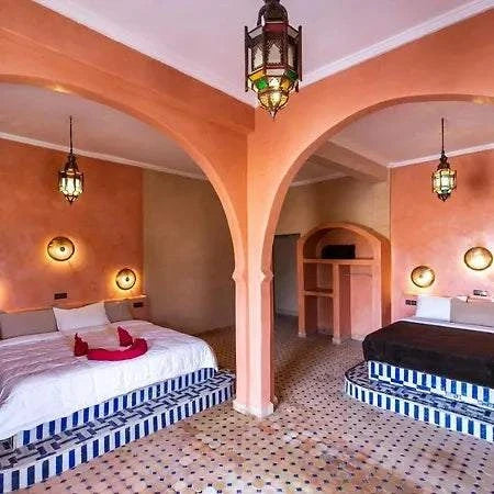 Hotel Nomad Palace room featuring two beds with striped blue and white bases, pink stucco walls, arched divider, and Moroccan lanterns