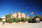Hotel Xaluca Dades clay-colored multi-story building with flagpoles displaying various national flags and a parked black off-road vehicle
