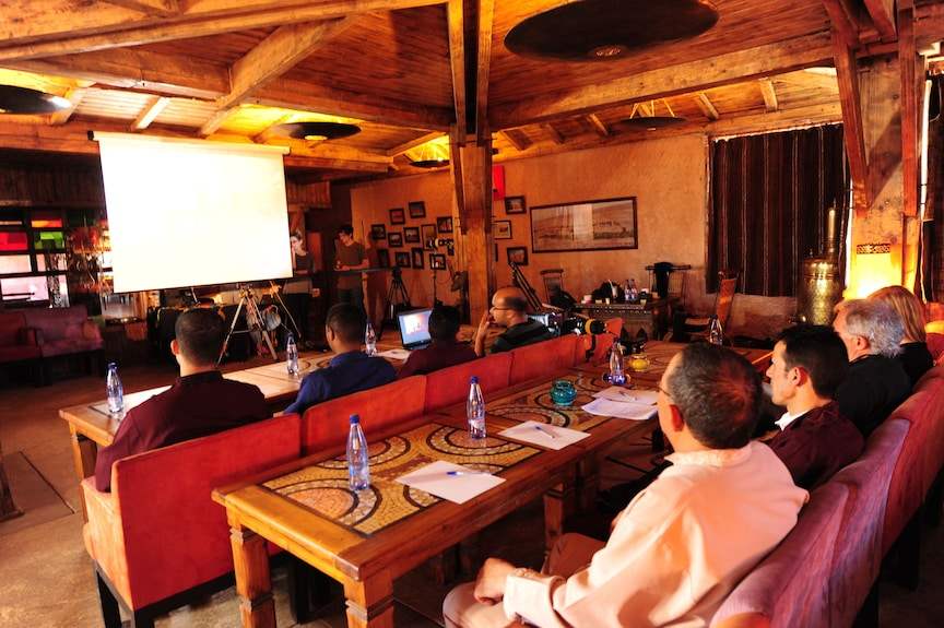 Hotel Xaluca Dades conference room with wooden beams, Moroccan decor, red upholstered seating, and attendees at tables with water bottles