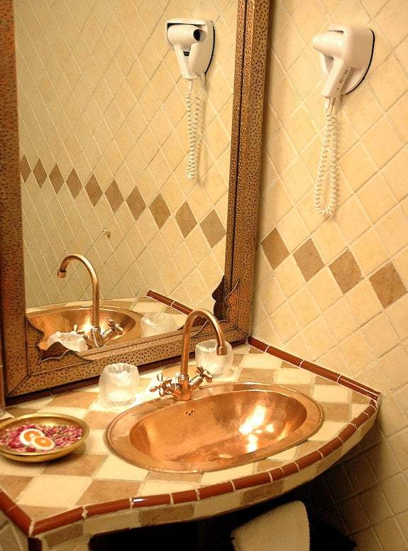 Hotel Xaluca Dades bathroom featuring a copper sink on a tiled countertop with beige and brown diamond-patterned walls and a mounted white hair dryer
