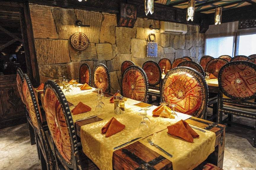 Hotel Xaluca Dades dining area with ornate wooden chairs featuring red and orange patterns, yellow tablecloths, and folded orange napkins