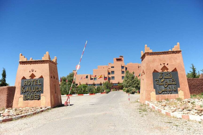 Hotel Xaluca Dades entrance with traditional Moroccan architecture in tan with stone signposts and clear blue sky