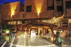 Hotel Xaluca Dades entrance at night with warm yellow lighting, traditional wooden awning, and people in white attire