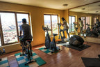 Hotel Xaluca Dades gym room with exercise bikes, wooden floor, large windows, and a scenic mountain view outside