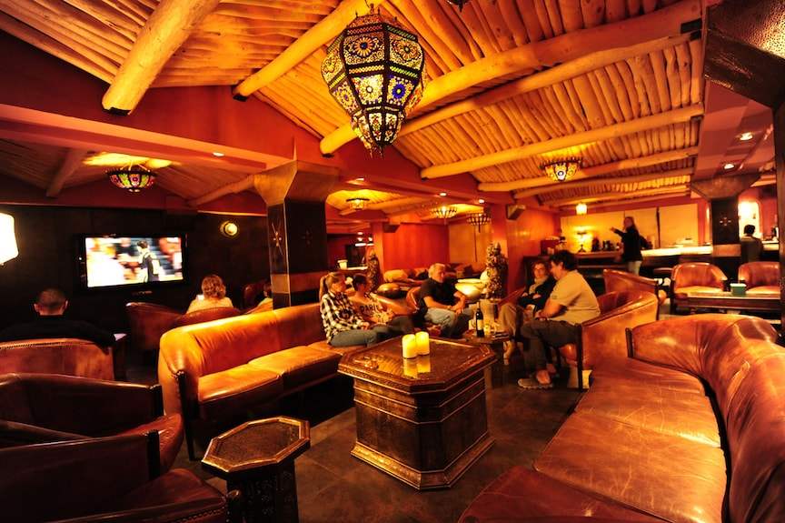 Hotel Xaluca Dades lounge area with warm orange walls, leather sofas, wooden ceiling beams, and Moroccan-style lamps