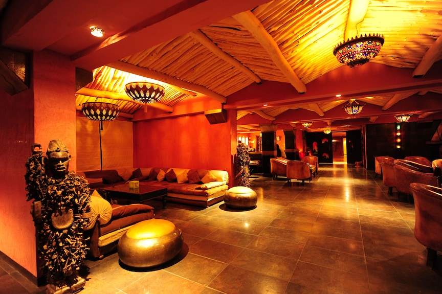 Hotel Xaluca Dades warm-toned lounge area with rustic wooden ceiling, comfortable brown sofas, traditional statues, and mosaic lamps