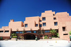 Hotel Xaluca Dades featuring pinkish-beige traditional Moroccan architecture with multiple terraces and a wooden entrance canopy against a clear blue sky