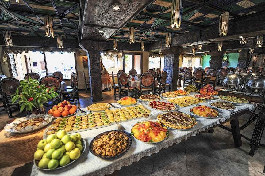 Hotel Xaluca Dades buffet table with a variety of colorful fresh fruits, pastries, and nuts in a traditional Moroccan dining room