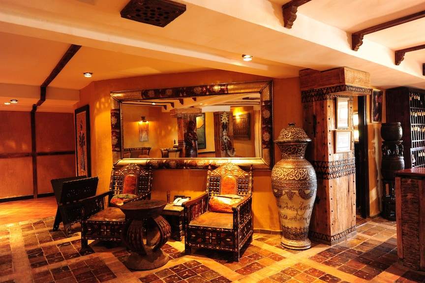 Hotel Xaluca Dades Moroccan style interior with warm earth tones, ornate wooden chairs, decorative pottery, and large mirror