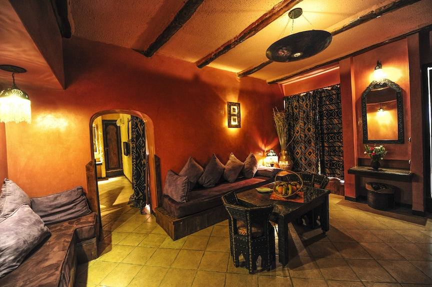 Hotel Xaluca Dades Moroccan style lounge with earthy orange walls, wooden furniture, patterned curtains, and purple cushions