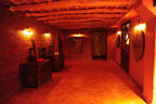Hotel Xaluca Dades traditional Moroccan interior hallway with terracotta tile floor, rustic wood ceiling beams, and decorative carved furniture