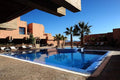 Hotel Xaluca Dades outdoor swimming pool with blue tiles surrounded by terracotta buildings and palm trees under clear blue sky