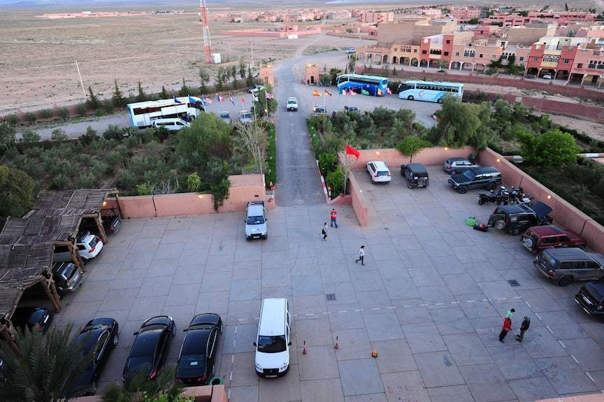 Hotel Xaluca Dades parking area with various vehicles including vans and cars in a paved lot surrounded by greenery and desert landscape