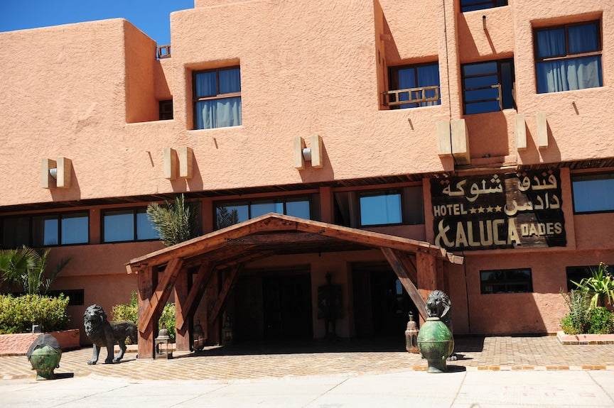 Hotel Xaluca Dades with peach-colored stucco facade, large windows, wooden entrance canopy, and lion statue at the front