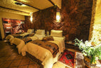 Hotel Xaluca Dades room with three single beds featuring white linens, brown patterned throws, stone walls, and terracotta tiled floor
