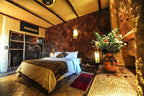 Hotel Xaluca Dades bedroom featuring rustic stone wall, wooden beams, white bedding, patterned throw, and vase with flowers