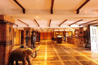Hotel Xaluca Dades interior with rustic wooden beams, yellow tiled floor, traditional Moroccan wood carvings, and elephant sculpture