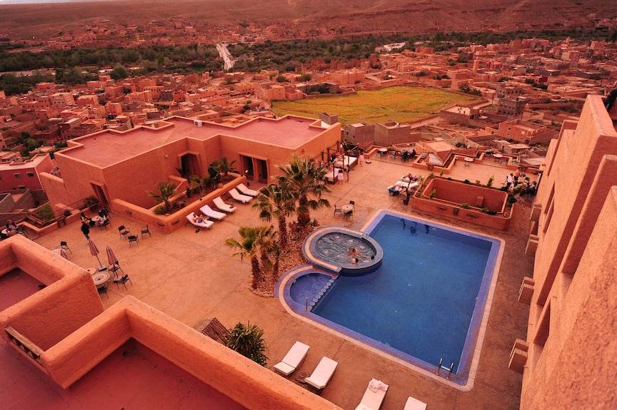 Hotel Xaluca Dades featuring terracotta buildings, outdoor swimming pool with Jacuzzi, palm trees, and lounge chairs