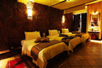 Hotel Xaluca Dades triple room with rustic stone walls, three single beds, beige and brown patterned throws, and warm lighting