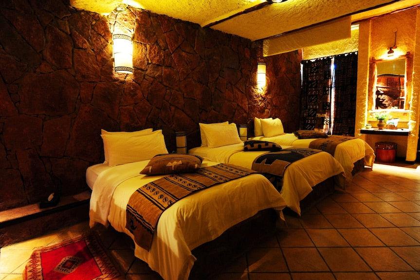 Hotel Xaluca Dades triple room with rustic stone walls, three single beds, beige and brown patterned throws, and warm lighting