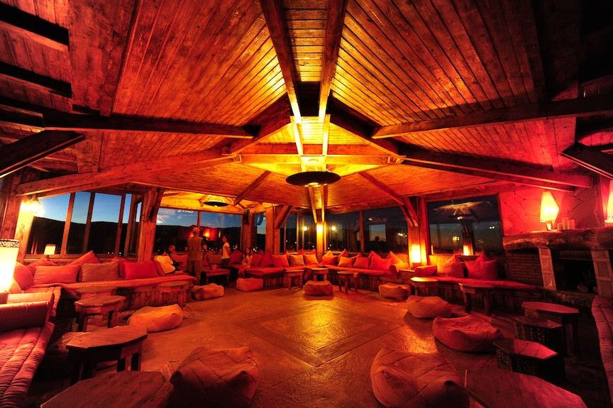 Hotel Xaluca Dades spacious lounge with warm wooden ceiling, soft orange cushions, low tables, and ambient lighting