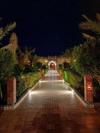 Hotel Yasmina Merzouga illuminated entrance pathway at night with lush green plants and ornate lanterns lining the tiled walkway
