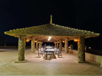 Hotel Yasmina Merzouga outdoor seating area at night featuring a large woven palm-thatched roof supported by column pillars with hanging lanterns