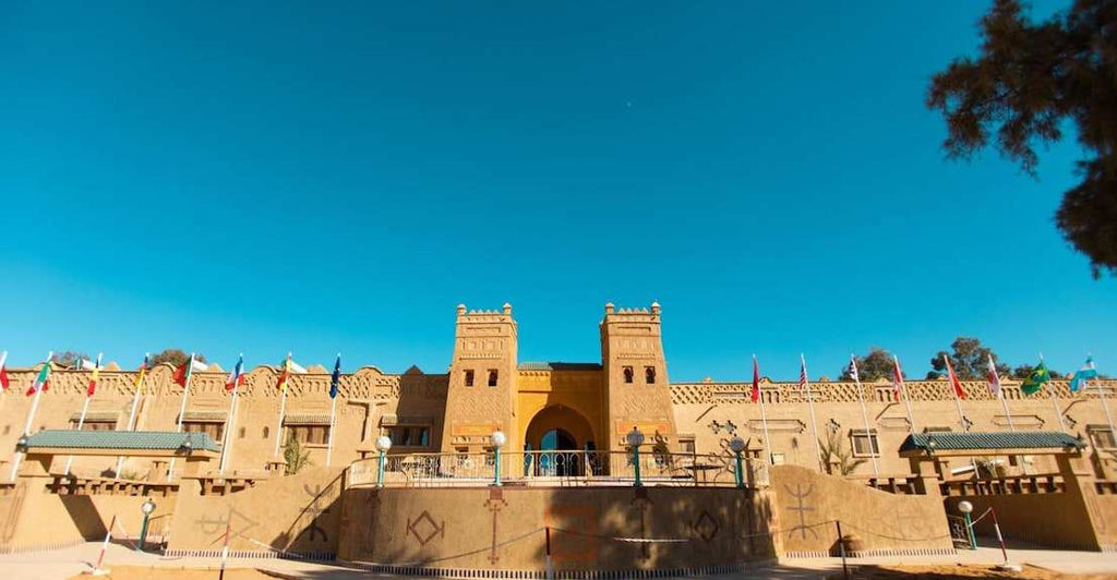 Hotel Yasmina Merzouga exterior featuring traditional Moroccan architecture in sandy beige with decorative patterns and multiple national flags