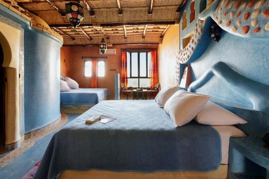 Hotel Yasmina Merzouga rustic bedroom with blue and orange walls, two beds with blue covers, and wooden ceiling