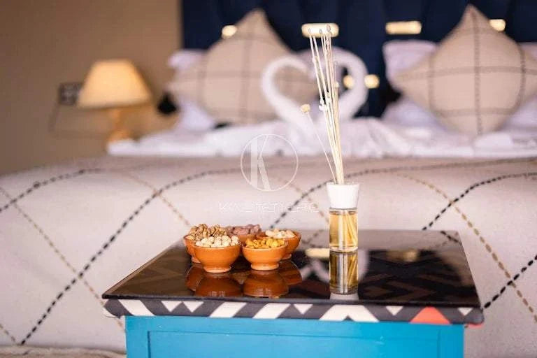 Kal Tenere Agafay luxury camp room featuring patterned bedspread, decorative pillows, black tray with snacks and reed diffuser