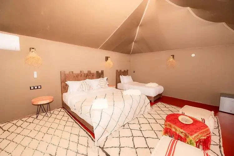 Kal Tenere Agafay luxury desert camp bedroom with two beds, beige walls, wooden headboards, patterned rugs, and warm lighting