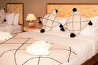 Kal Tenere Agafay luxury desert camp bedroom with beige and black geometric patterned blankets and cushions on double beds with wooden headboards
