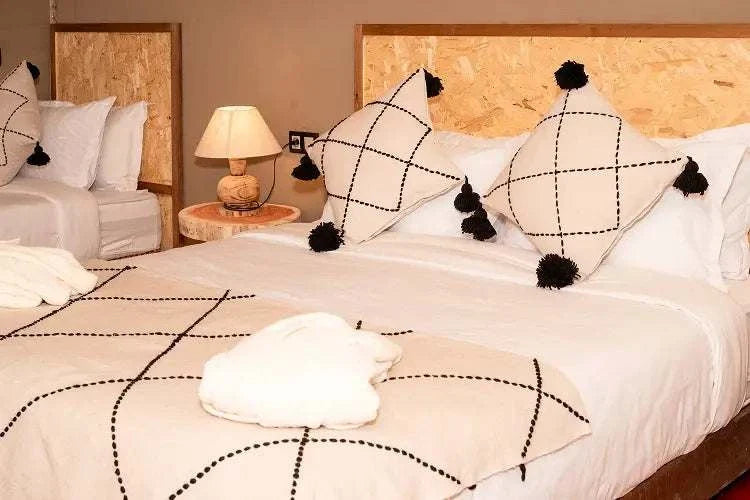 Kal Tenere Agafay luxury desert camp bedroom with beige and black geometric patterned blankets and cushions on double beds with wooden headboards