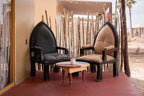 Kal Tenere Agafay luxury desert camp featuring two cushioned wooden armchairs in black and beige with a small round table on a red patio