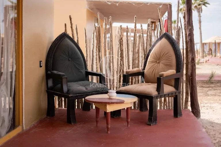 Kal Tenere Agafay luxury desert camp featuring two cushioned wooden armchairs in black and beige with a small round table on a red patio