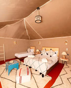 Kal Tenere Agafay luxury desert camp interior with tan fabric walls, queen and twin beds, patterned rugs, and Moroccan decor
