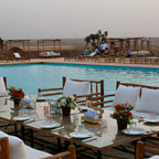 Kal Tenere Agafay luxury desert camp outdoor dining table with white cushions, floral centerpieces beside a turquoise swimming pool