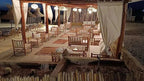 Kal Tenere Agafay outdoor luxury desert camp seating area with wooden chairs, beige cushions, rugs, and hanging lanterns